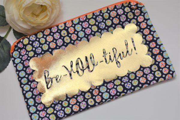 Zipper Pouch, Front: 'Be-YOU-tiful' silhouette in scalloped gold vinyl on navy fabric with white polka dots filled with colorful dot designs; orange zipper