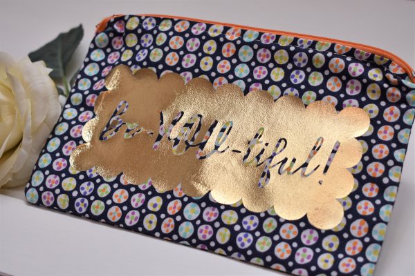 Zipper Pouch, Front: 'Be-YOU-tiful' silhouette in scalloped gold vinyl on festive navy fabric; orange zipper